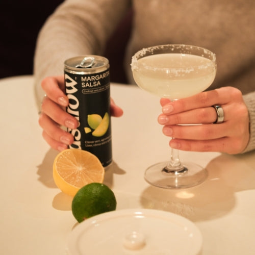 Persona in possesso di un mocktail di salsa Margarita e di una lattina, con lime e limoni freschi su un tavolo.